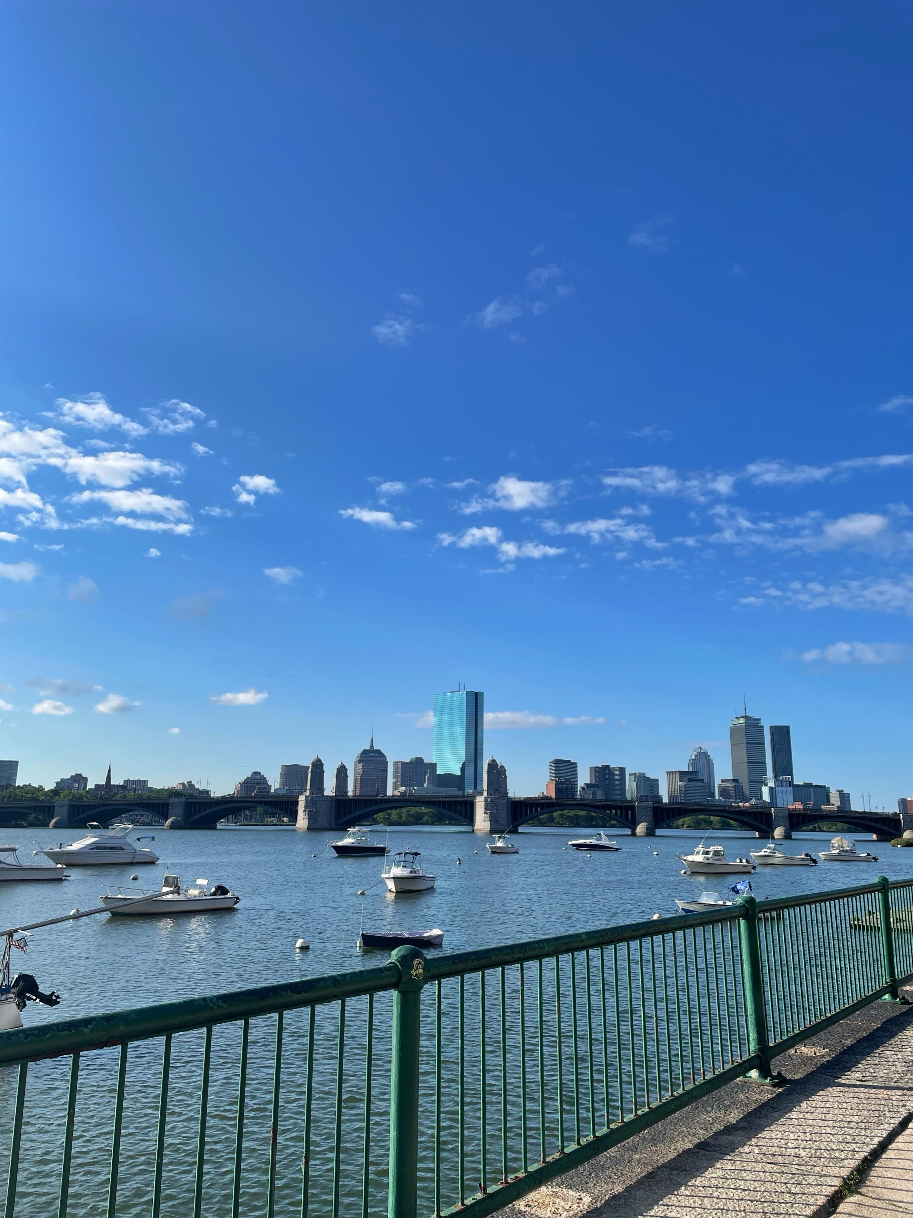 Calm Sunday morning view of boats on the Charles River with a clear blue sky and the Boston skyline in the background.