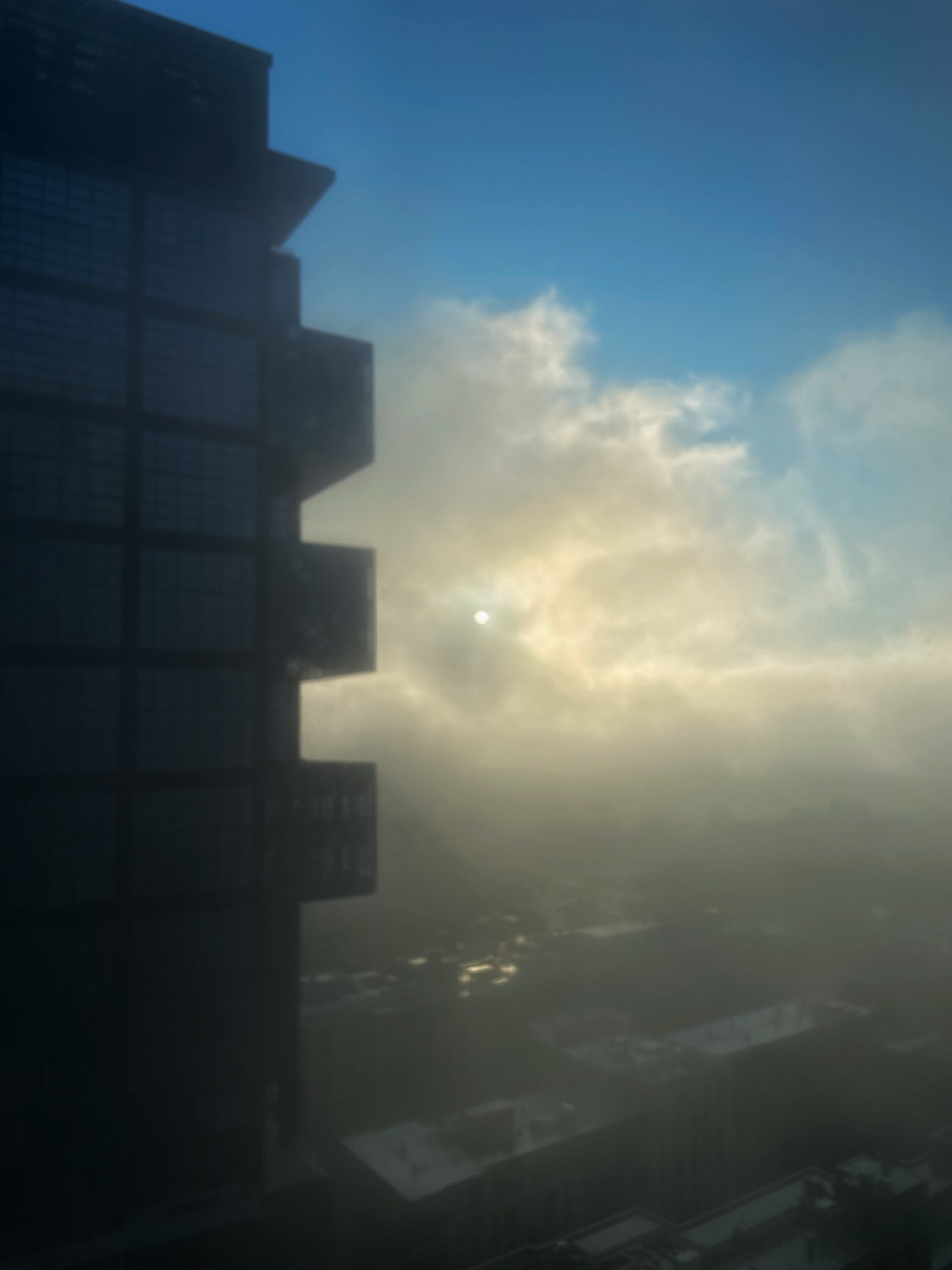 Early Friday morning view of a tall glass building with fog drifting across the city and soft sunlight glowing through the haze.